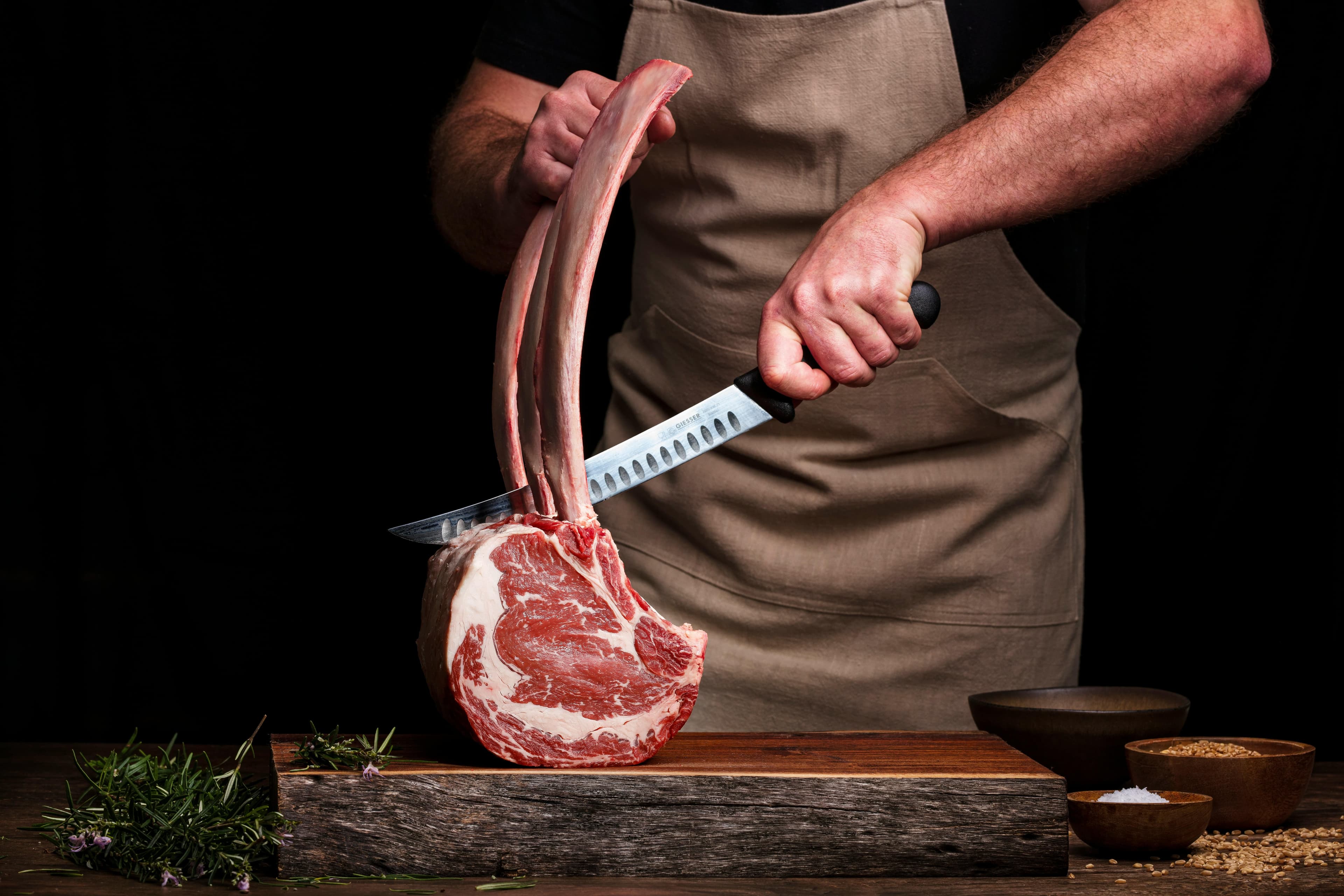 Chef carving a tomahawk ribeye with butcher's knife