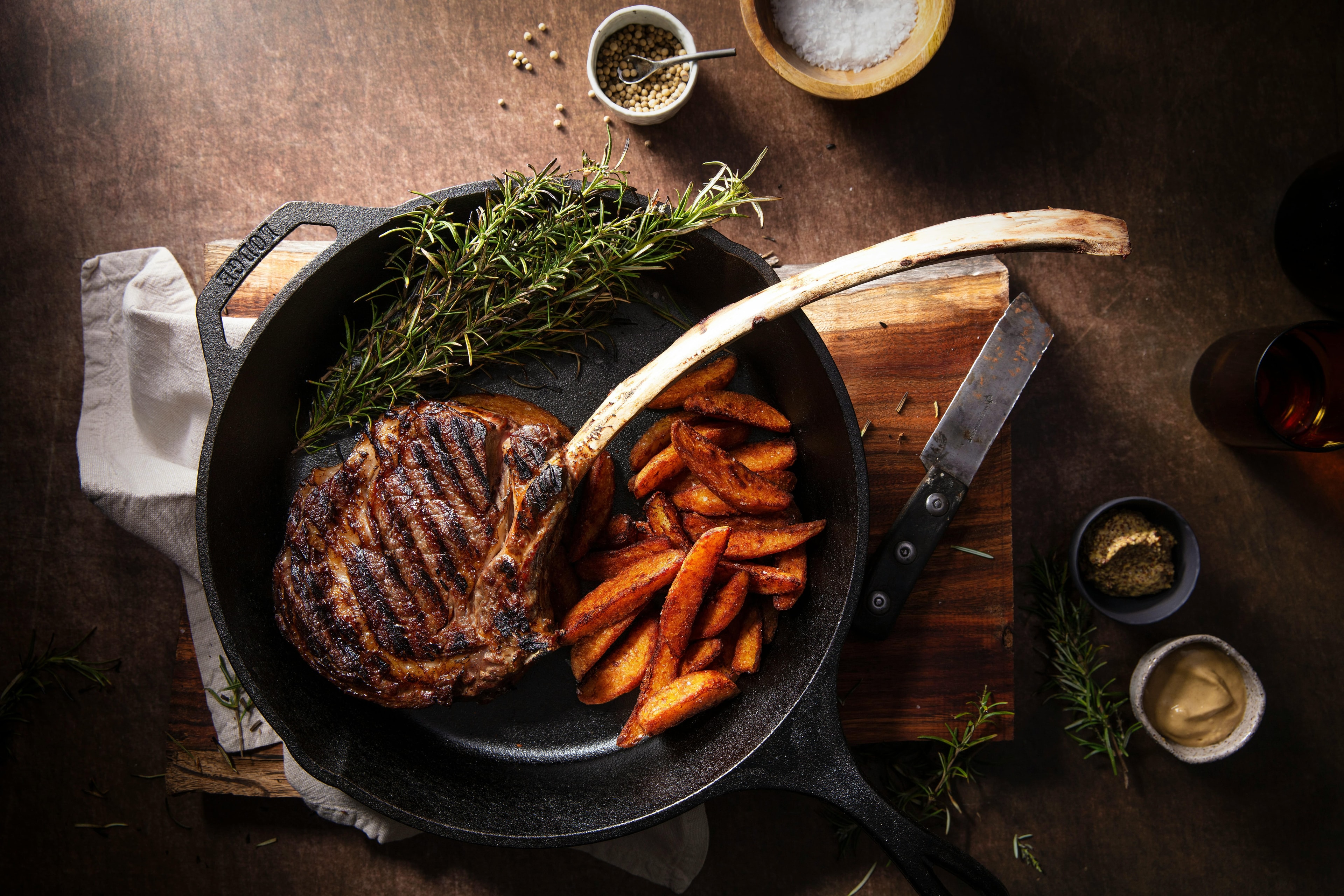 Tomahawk steak served in cast iron skillet with potato wedges and rosemary